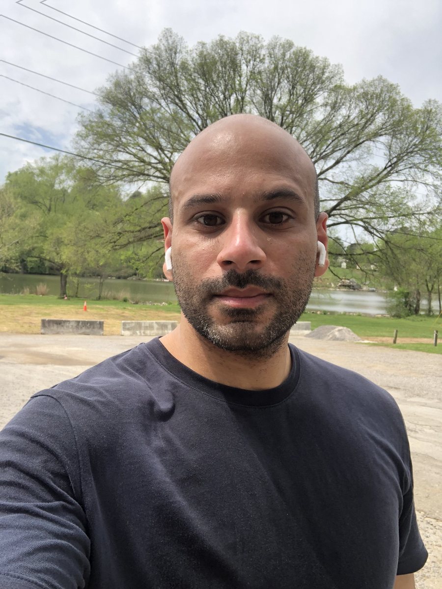 Malek Damiri in a navy t-shirt in a park with a large tree behind him